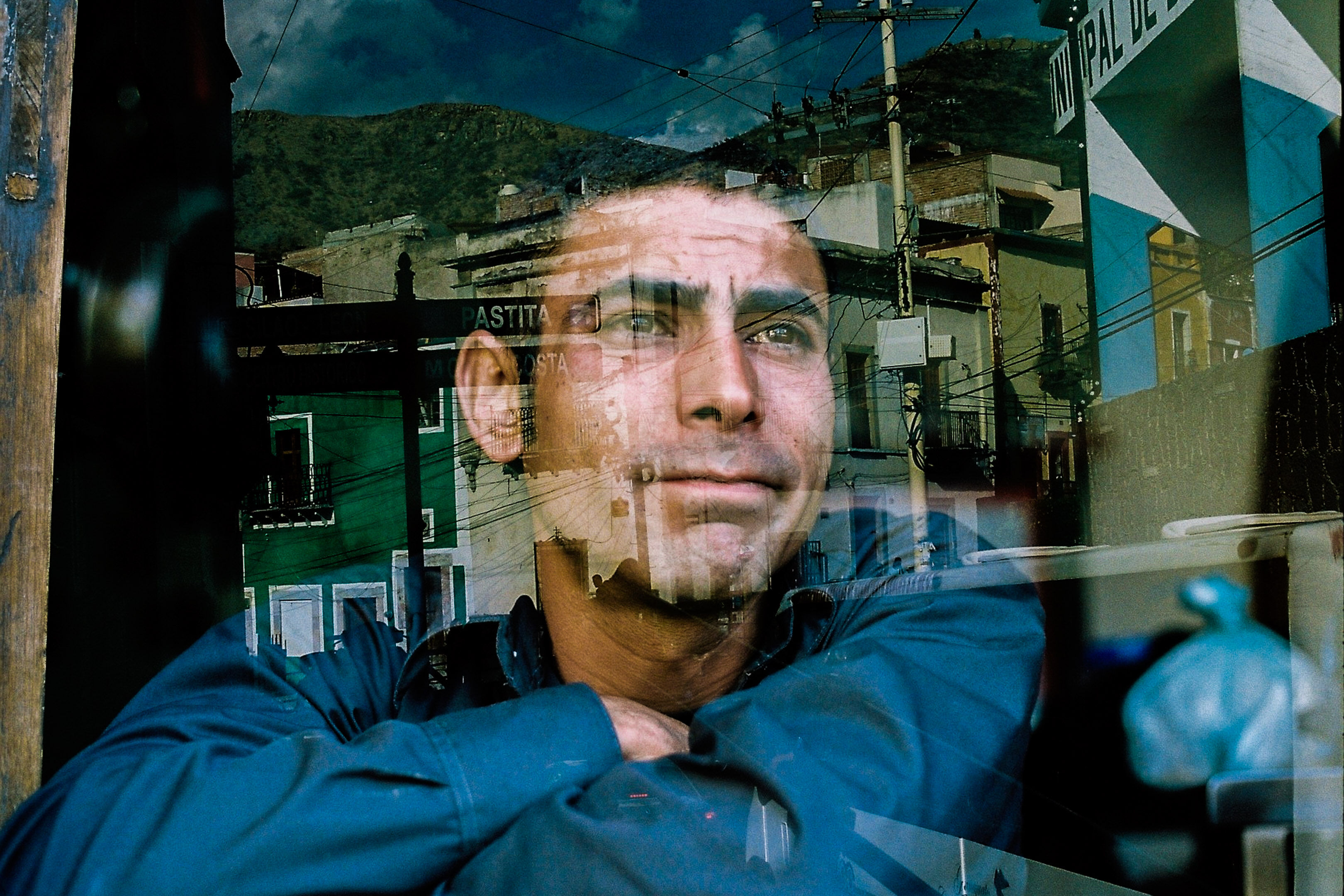 Double exposed image of a melancholic man staring out of a window and an overlay of different colored houses of a village in the mountains