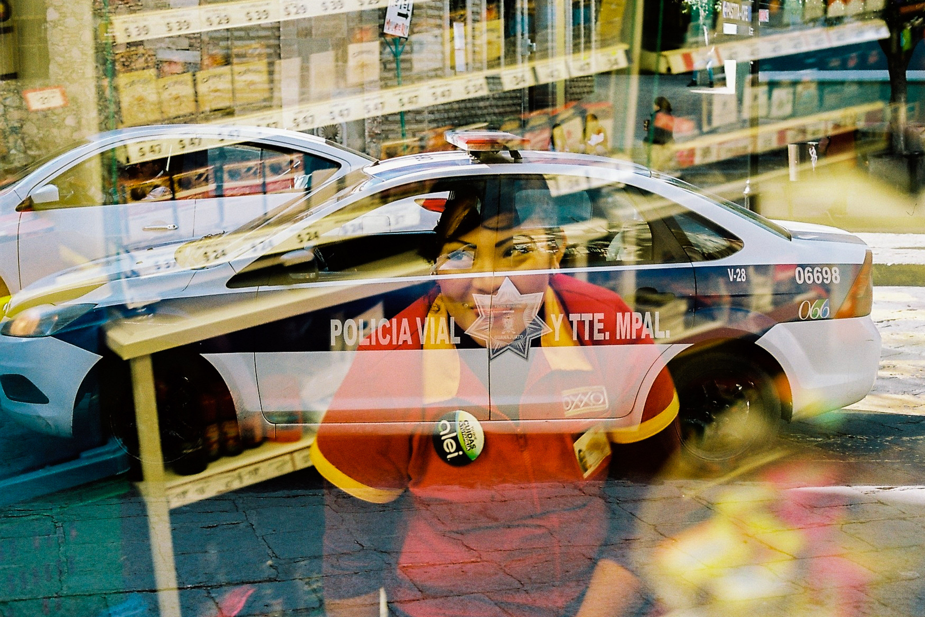 Double exposed image of a woman in an oxxo shirt with a police car in the backround